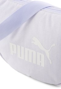 Geanta sport de culoare violet deschis, realizată dintr-un material texturat. Prezintă un mare logo alb "PUMA" și o siluetă a unei feline săltând.