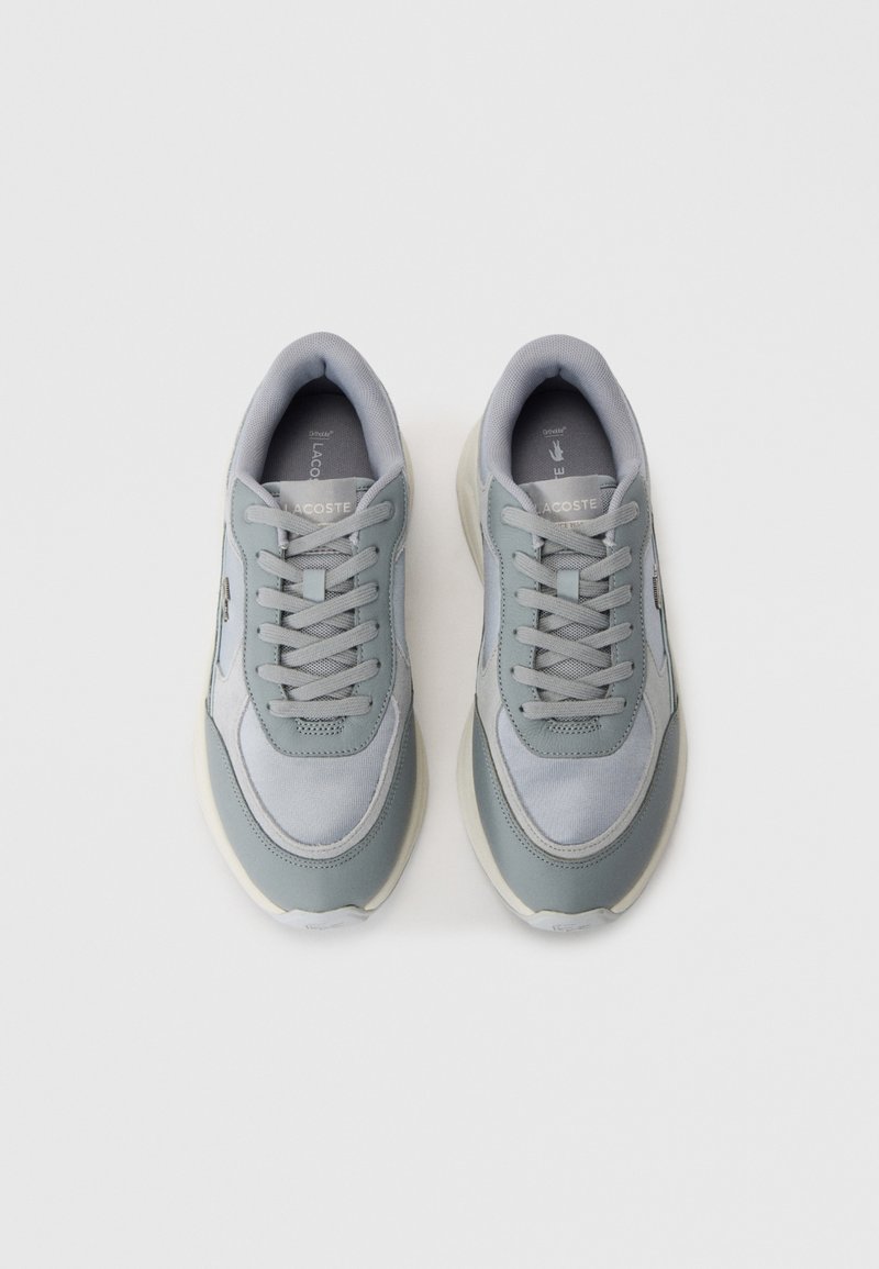 Une paire de baskets Lacoste gris clair avec des semelles et des lacets blancs, vue de dessus sur un fond blanc.