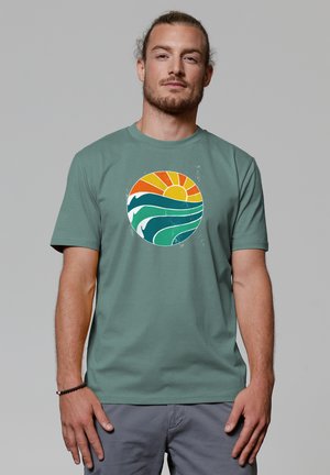 Groene katoenen t-shirt met een ronde afbeelding van een oranje zon en golven in turquoise en wit. Korte mouwen, casual pasvorm.