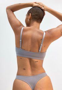 Grauer Bikini in zwei Teilen mit dünnen verstellbaren Trägern, glatter Textur und minimalistischem Design. Mit dezenten Tätowierungen auf dem Rücken.