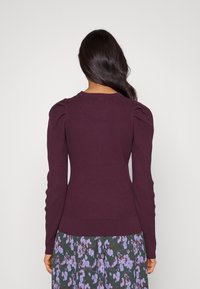 Mörkröd ribbad tröja med puffärmar och rund halsringning, som bärs tillsammans med en blommig kjol med lila och gröna mönster.