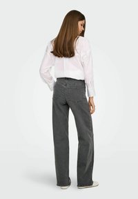 Hallid kõrge vöökohaga laiad teksad halli värviga, sujuva tekstuuriga, viie taskuga ja kontrastsete õmblustega, kombineeritud valge nööpidega särgiga.