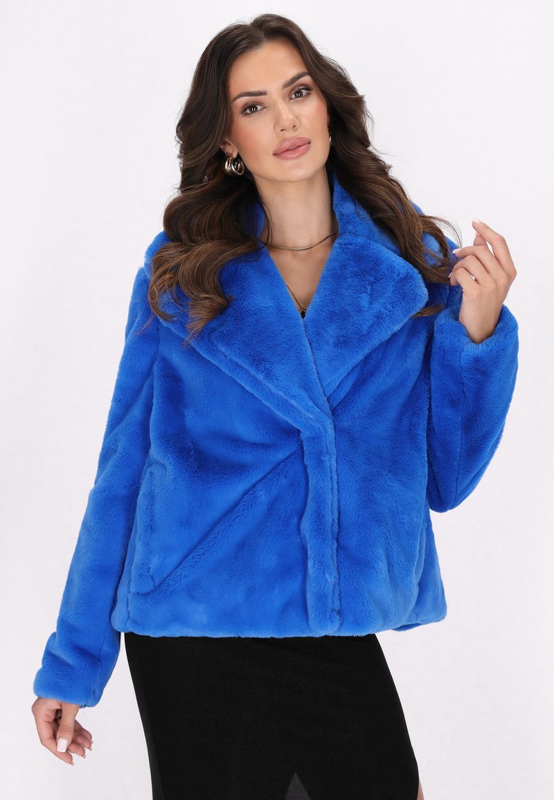 Faux fur jacket in vibrant blue, featuring a shawl collar, long sleeves, and a structured design with diagonal seams. Soft texture overall.