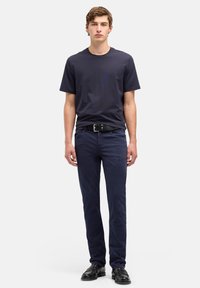 Maglietta di cotone blu navy, collo rotondo, abbinata a pantaloni blu navy, vestibilità dritta, con cintura nera e scarpe di pelle nere.