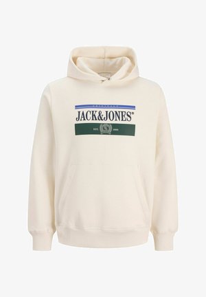 Chłopiec z kręconymi włosami, ubrany w kremową bluzę z kapturem Jack & Jones, białą koszulę, szerokie niebieskie dżinsy i beżowe buty, stojący na białym tle.