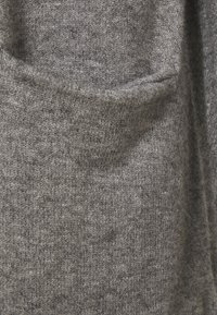 Suéter gris de punto con textura, bolsillo redondeado y apariencia suave y cálida, ideal para usar en capas en climas más frescos.