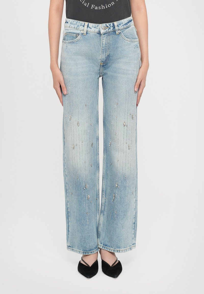 Licht gewassen denim wijde broek met versieringen, voorzien van zilveren accenten en vervaging. Gepaard met zwarte puntige schoenen.