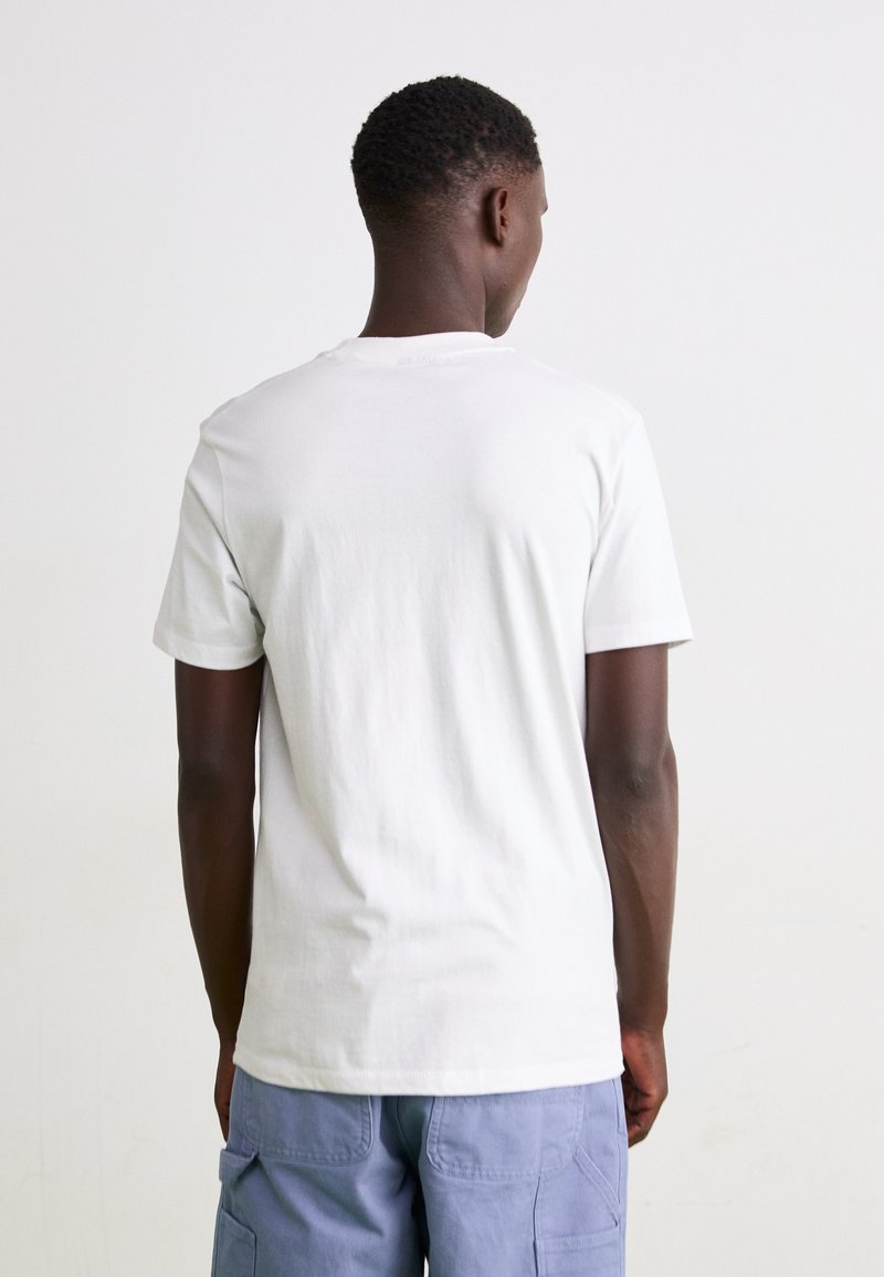 Biała bawełniana koszulka z okrągłym dekoltem, krótkimi rękawami i gładką fakturą. Nosi ją osoba widziana z tyłu, w połączeniu z niebieskimi spodniami cargo.