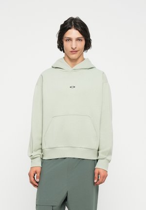 Hanorac verde deschis cu un buzunar tip kangaroo în față, cu mansete și margine ribbate. Are un mic logo pe piept. Textură netedă, croială lejeră.