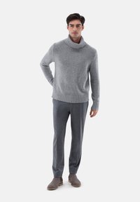 Grauer Strickpullover mit hohem Rollkragen, gerippten Bündchen und Saum, kombiniert mit grauen Hosen und grauen Wildleder-Stiefeletten. Schlichter Hintergrund.