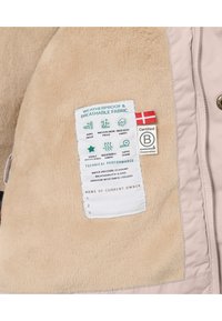 Giacca in pile beige con un'etichetta di cura del tessuto che mostra le caratteristiche impermeabili, inclusi isolamento, traspirabilità e cuciture nastrate.