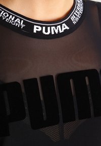 Czarna przezroczysta bluzka z wyraźnym welwetowym logo "PUMA". Kołnierz elastyczny, z białymi literami wplecionymi w materiał. Miękka w dotyku.