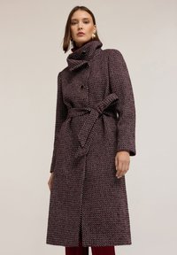 Cappotto a fantasia bordeaux e bianco con colletto alto, design doppiopetto e cintura annodata in vita. Tessuto morbido e texturizzato.