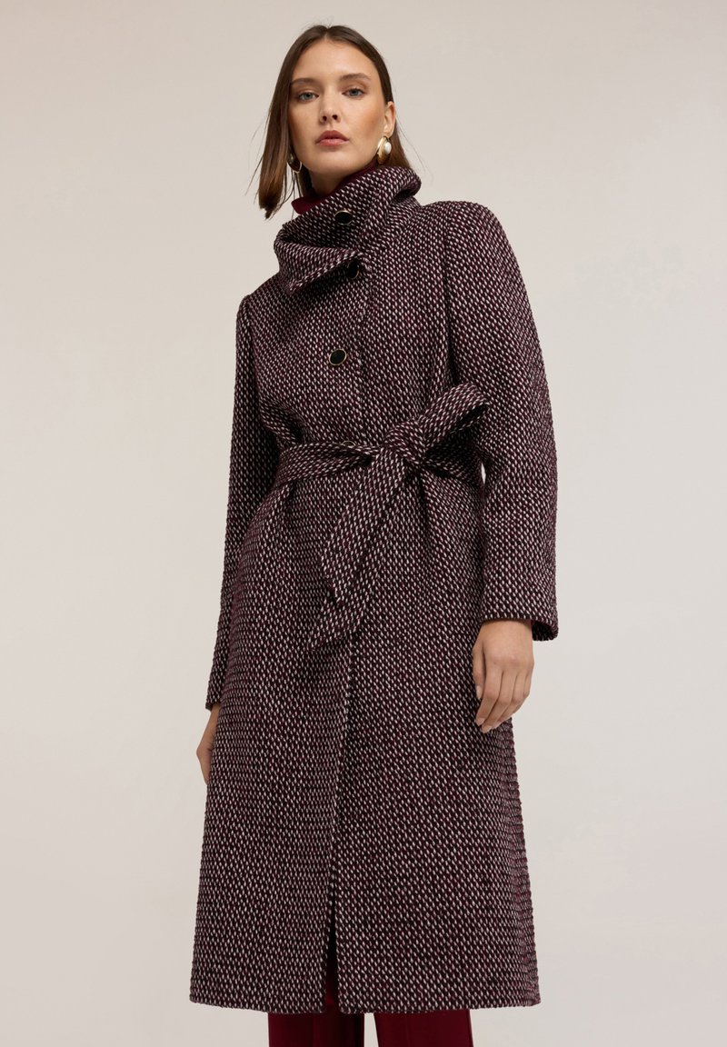 Cappotto a fantasia bordeaux e bianco con colletto alto, design doppiopetto e cintura annodata in vita. Tessuto morbido e texturizzato.