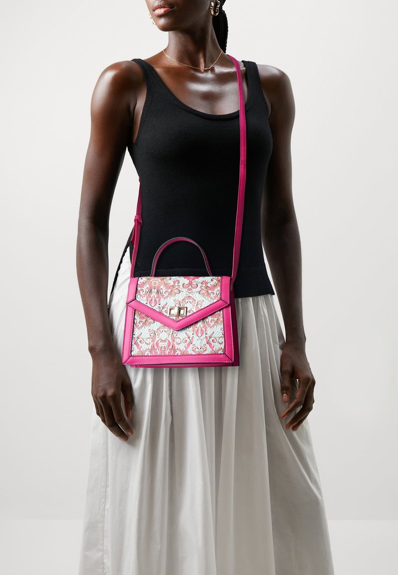Femme portant un haut noir sans manches et une jupe blanche, portant un sac bandoulière rose et blanc à motifs.