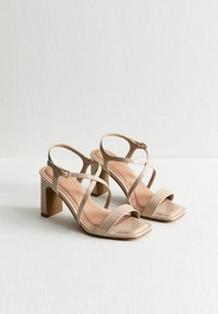 Beige hoge hakken sandalen met meerdere kruisschoenen, een vierkante neus, een gladde afwerking en een chunkyt blokhak. Gesp sluiting op de enkelband.