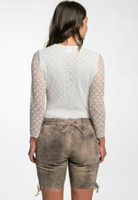 Spitzenoberteil mit langen Ärmeln und Rautenmuster, kombiniert mit taupefarbenen Wildleder-Shorts mit gebundenem Bund und seitlichen Akzenten, die einen strukturierten Look kreieren.