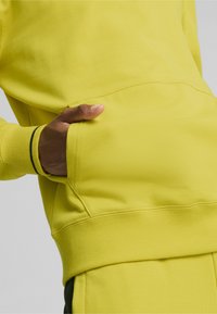 Ljust gul sweatshirt med känguruficka, ribbade muddar och nederkant, med en mjuk textur och minimalistiska designdetaljer.