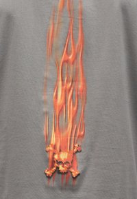 Πορτοκαλί φλόγα με ένα καίγον κρανίο και σταυρωμένα οστά στο κέντρο σε φόν γκρι ύφασμα.