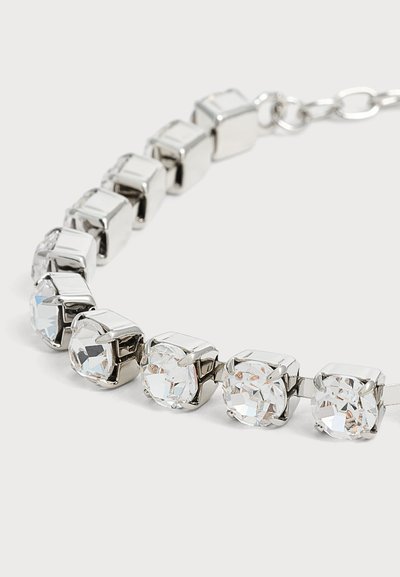 Gros plan d'un bracelet en argent avec des pierres précieuses carrées et transparentes enchaînées en rang sur un fond clair.