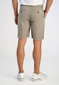 Bermudas caqui con un patrón texturizado, dos bolsillos traseros y los dobladillos rematados. Combinadas con zapatillas deportivas blancas, mostrando un estilo claramente casual.