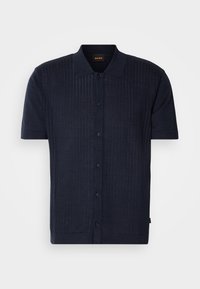 Chemise en maille bleu marine à manches courtes avec col et boutons sur le devant, présentant de subtiles rayures verticales texturées et une petite étiquette de marque à l'intérieur du col.