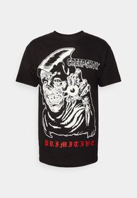 Camiseta de algodón negra con un gráfico blanco de una criatura sosteniendo un objeto, con el texto "CREEPSHOW" y "PRIMITIVE" en rojo.