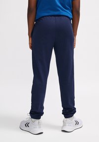 Marine joggers met elastische boorden en tailleband, gemaakt van zachte materialen. Gecombineerd met witte sportschoenen met zwarte accenten.