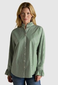 Cămașă cu dungi verzi și albe, cu guler și manșete volă, confecționată din țesătură de bumbac. Prezintă o croială lejeră și detalii subtile.