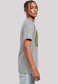 Camiseta de algodón gris con mangas cortas y cuello redondo, que presenta un diseño gráfico verde en la parte frontal.