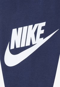 Material din stofă albastru marin cu un logo mare Nike alb, cu design swoosh. Textura este netedă, iar materialul pare moale.