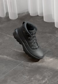 Czarne outdoorowe buty z wyściełanym kołnierzem, skórzaną cholewką o teksturowanej powierzchni, płaskimi sznurówkami z białymi akcentami oraz solidną gumową podeszwą.