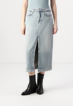 Jupe en denim bleu clair avec une fente à l'avant, longueur mi-longue et bords ourlés. Associée à des bottines montantes en cuir noir.