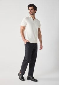 White short-sleeve polo shirt with a v-neck, paired with black slim-fit trousers and black lace-up shoes. Simple design, ribbed texture.