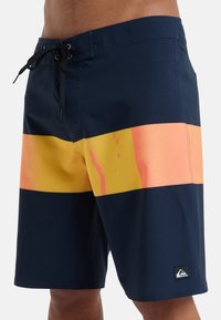 Námornícke modré plavky so širokými pruhmi v oranžovej a žltej farbe. Sťahovanie na šnúrku s logom na spodnej časti nohy.