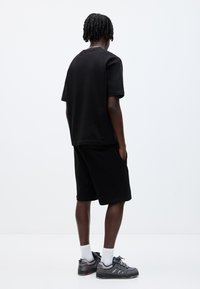 Sort kortærmet T-shirt og sorte shorts i bomuldsblanding med en afslappet pasform. Har sidelommer og enkel syning, sat sammen med mørke sneakers.