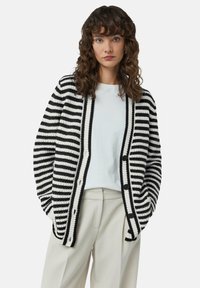 Schwarz-weißer gestreifter Cardigan mit strukturiertem Strick, runder Ausschnitt, Knopfverschluss und zwei Taschen. Mit einem hellen Oberteil kombiniert.