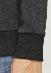 Donkergrijze sweatshirt manchette in een gestructureerde stof met gebreide details. Zichtbare hand en denim stof net boven de manchette.