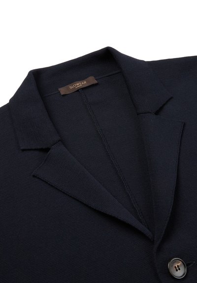 Navy knit blazer with notched collar, button closure, and visible stitching detail. Label reads "Slowear" attached at the neckline.
