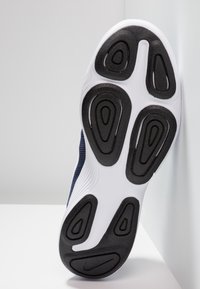 Zapatilla deportiva con suela de goma negra que presenta ranuras curvadas, entresuela blanca y parte superior de material texturizado en color azul marino.