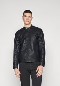 Chaqueta de cuero negra con un cuello alto, cierre de cremallera y detalles de costura mínimos. Presenta mangas largas y una silueta ajustada.