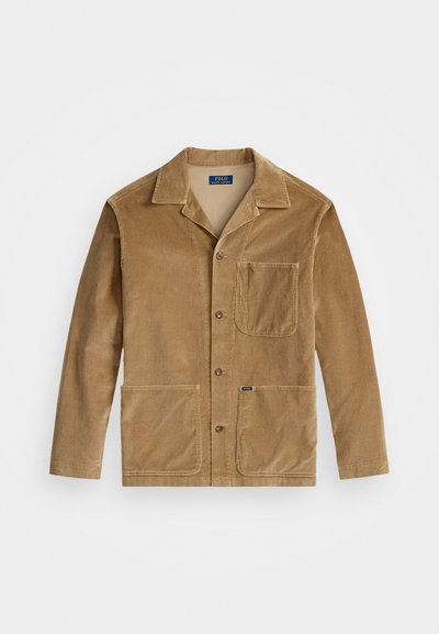 Varinės spalvos kordūroji striukė su apykakle, priekyje užsegama mygtukais ir dviem didelėmis kišenėmis. Taip pat turi krūtinės kišenę ir logotipo detalę.