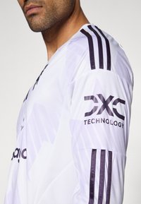 Camisola desportiva branca de manga comprida com detalhes em roxo. Apresenta a marca "DXC Technology" em preto na manga e três riscas no ombro.