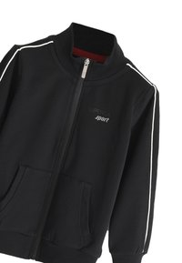 Schwarze Zip-Jacke aus weichem Material, mit weißen Seitenstreifen, hohem Kragen und zwei Fronttaschen. Logo auf der Brust.