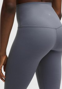 Leggings atléticos de cintura alta en un tejido gris oscuro sólido, con una textura suave y costuras planas, presentando un logo cerca de la cinturilla.