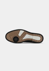 Suola di scarpa elegante nera con battistrada marrone e bianco, impugnatura circolare nera vicino al tacco e "BOSS" impresso in un pannello di gomma bianca.