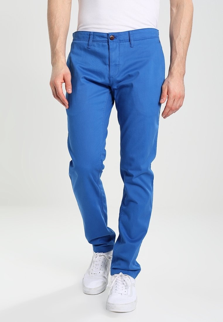 Modré chino kalhoty vyrobené z bavlny, zúžený střih, střední výška pasu, s jedním uzávěrem vpředu na knoflík a dvěma bočními kapsami. V kombinaci s bílými teniskami.