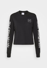 Sort langærmet croptop i bomuld med en lille hvid logo på brystet og "Huf Worldwide" i hvid ned langs venstre ærme.