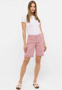 Shorts en denim rose avec ourlets retroussés, poches avant, fermeture à bouton, et un tissu légèrement extensible ; assortis à un haut blanc à manches courtes.