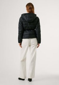 Zwarte pufferjack, met een capuchon, gequilt textuur en een getailleerde taille. Gecombineerd met witte wijde broek en zwarte haklaarzen.